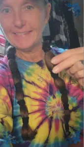 A woman in a tie-dye shirt holding a ponytail tied up with several bands.