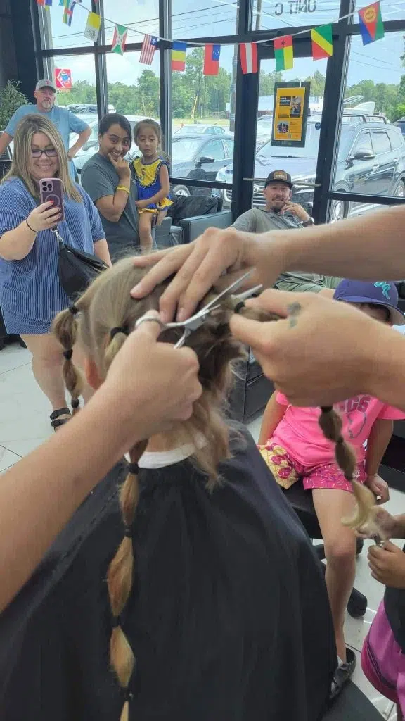 Pryor's hair is divided into several ponytails as his father begins cutting the donation, while family and friends gather to witness the special moment benefiting Wigs For Kids.